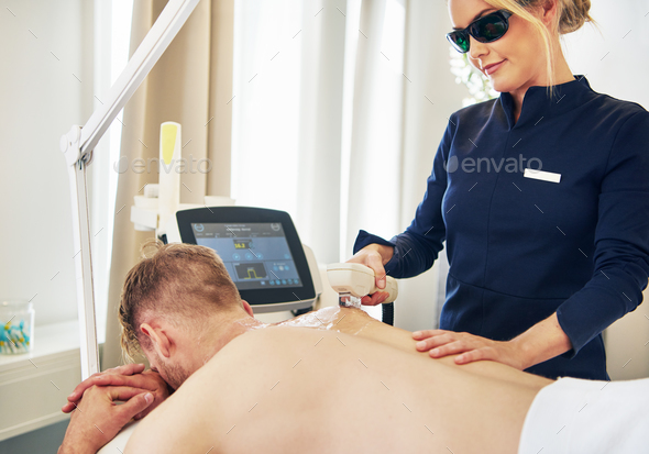 Young beauty technician performing laser hair removal on a client